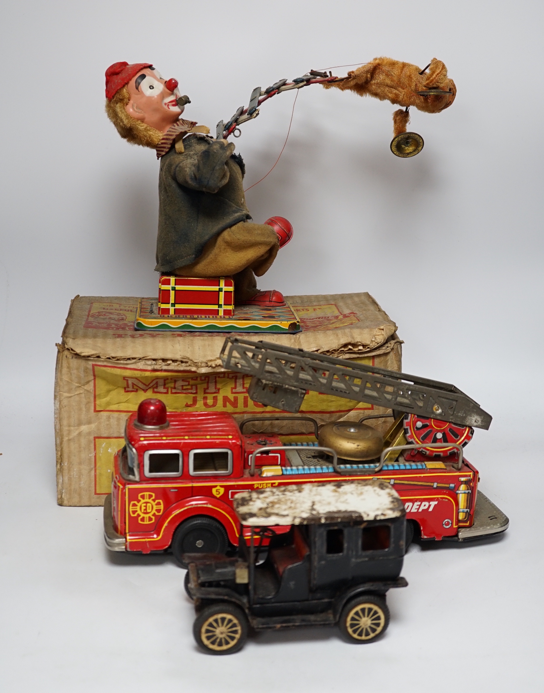 Four tinplate toys; a model of a 1920s taxi, a 1960s German made fire engine, an automaton clown, and a boxed Mettype Junior children’s typewriter